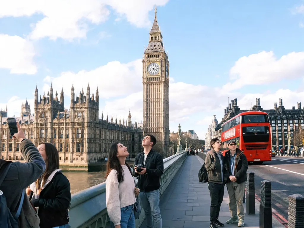 Turyści na moście Westminster podziwiają Wieżę Elizabeth i Big Ben w słoneczny dzień, w tle gmach Parlamentu i czerwony autobus
