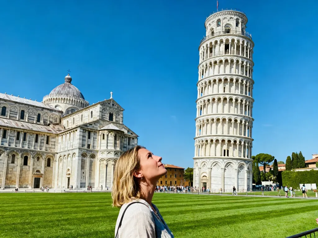 Turystka podziwiająca Krzywą Wieżę w Pizie na tle błękitnego nieba i zabytkowego placu Piazza dei Miracoli.