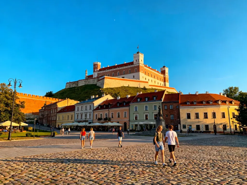 Słoneczny Plac Zamkowy w Lublinie z widokiem na majestatyczny zamek wznoszący się na wzgórzu.