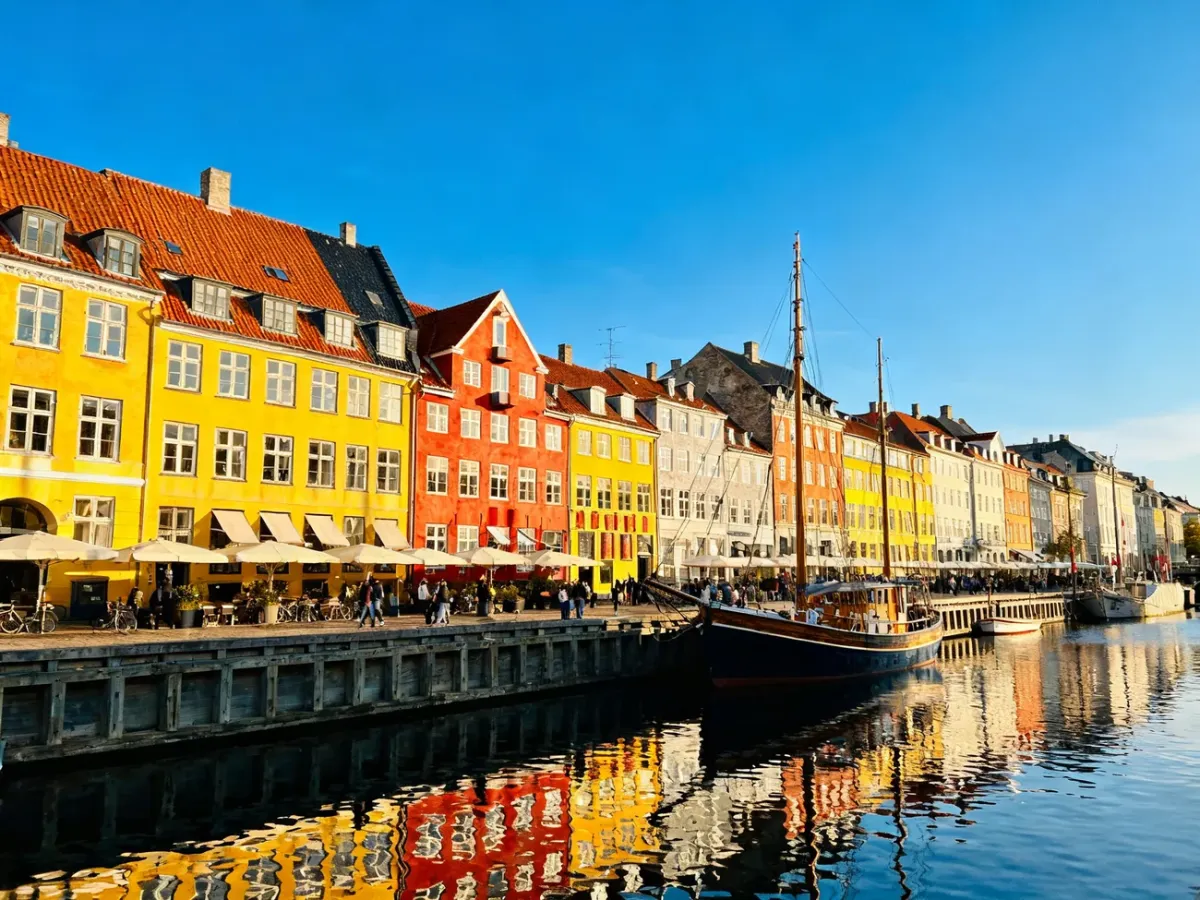 Kolorowe kamienice nad kanałem Nyhavn w Kopenhadze w słoneczny dzień. Drewniana łódź zacumowana przy nabrzeżu.